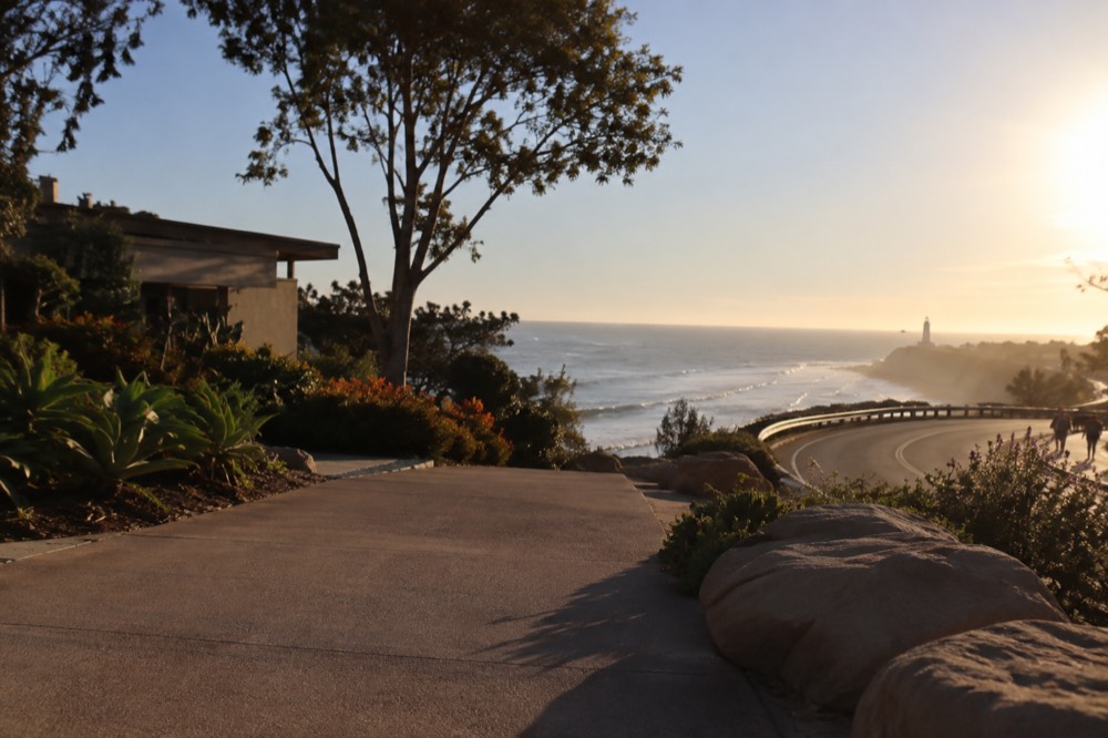 Coastal highway curve with ocean views and a lighthouse silhouette in the distance