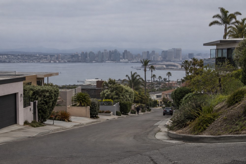 Winding road climbing a hillside through houses with ocean glimpses