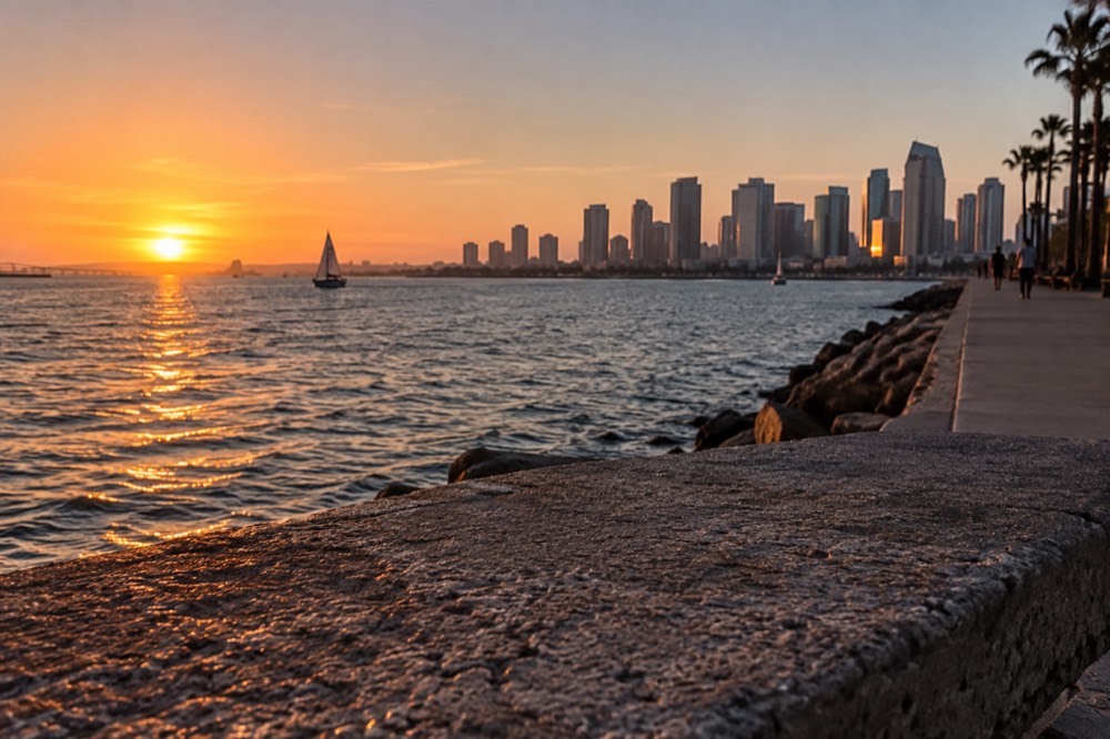 Sun sinking into the ocean with a city skyline glowing pink in the opposite direction