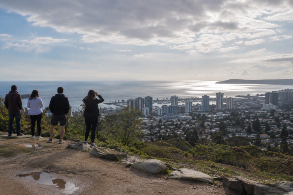 People standing at an open hilltop overlook looking out over the ocean horizon