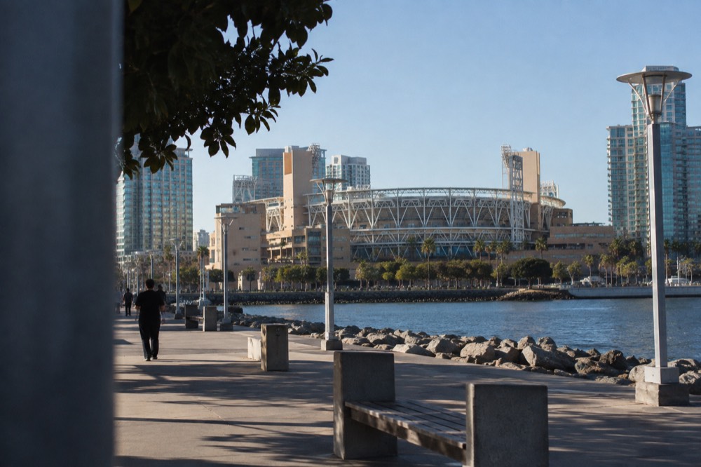 A waterfront baseball stadium with a white steel facade and palm trees under a blue sky