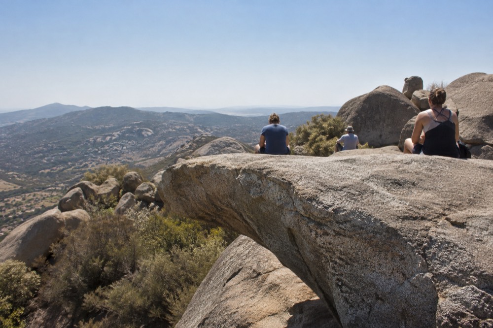 Hikers resting on large granite boulders along an open ridgeline under a clear sky