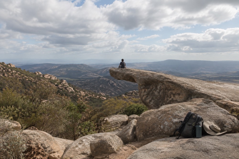 A backpack, water bottles and a hat resting on a rock beside a trail
