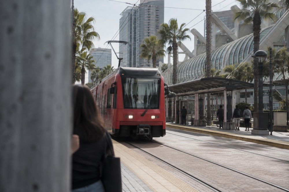 Red trolley arriving at a downtown station with a modern convention hall in the background