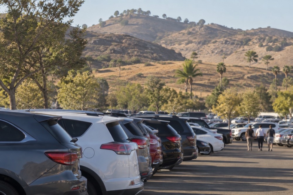 Rows of parked cars in a sunlit parking lot with hills in the background