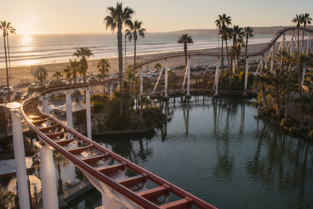 A steel roller coaster track curving over a lagoon with palm trees