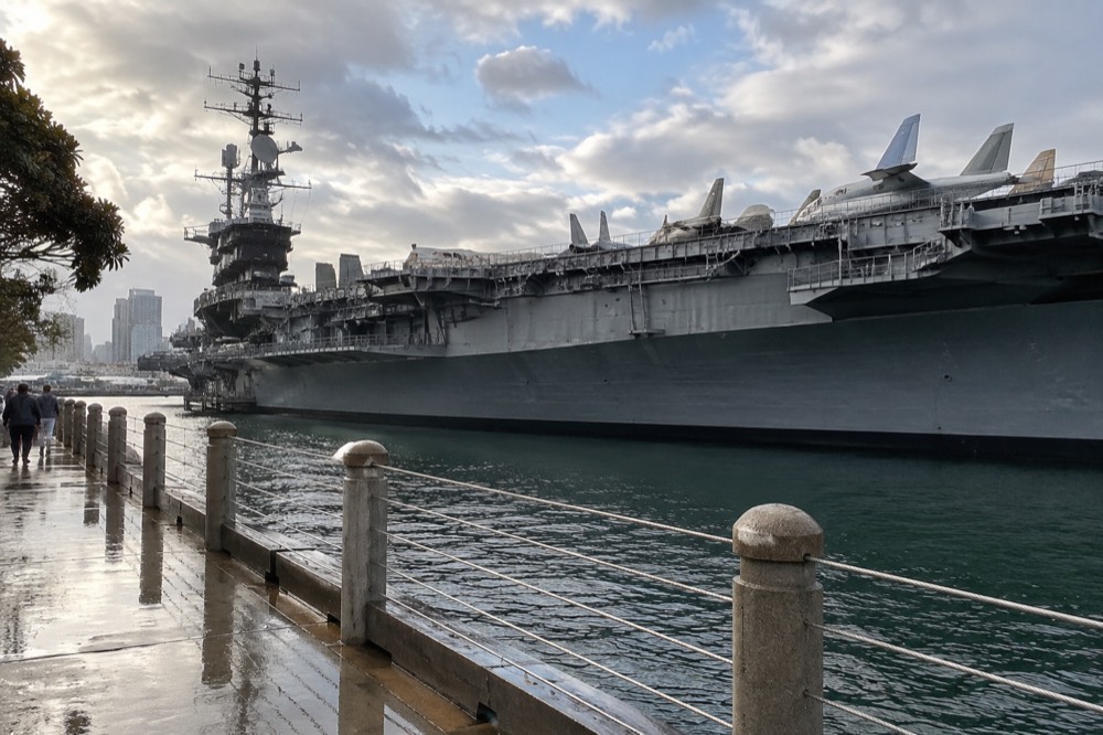 An aircraft carrier museum moored at a downtown waterfront with aircraft on its flight deck