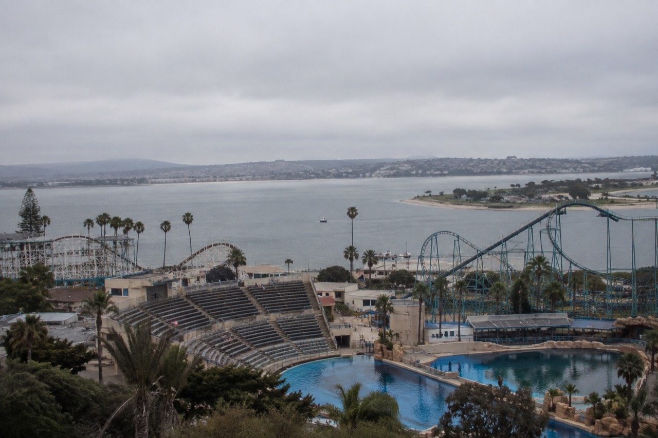 Aerial view of a marine park with a large bay, roller coaster tracks, and stadium seating