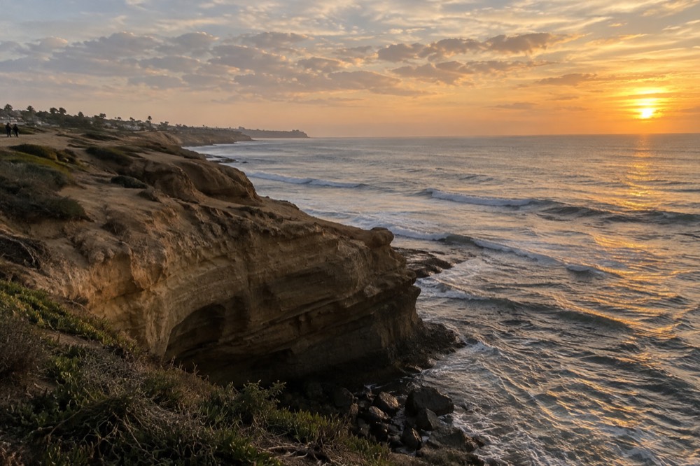 Golden evening light over ocean bluffs with a wide horizon and scattered clouds
