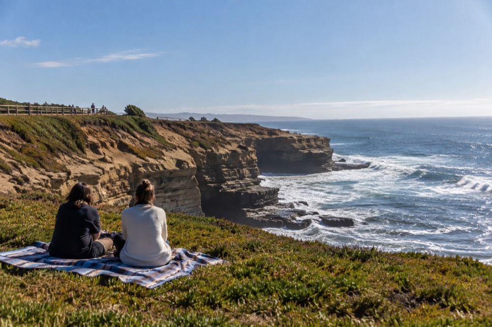 Picnic blanket on grass near a bluff edge with the ocean beyond