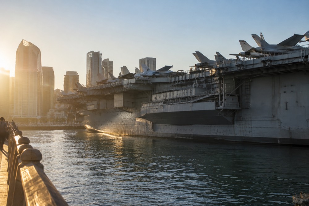 Restored military aircraft lined up on the aircraft carrier's flight deck with downtown buildings behind