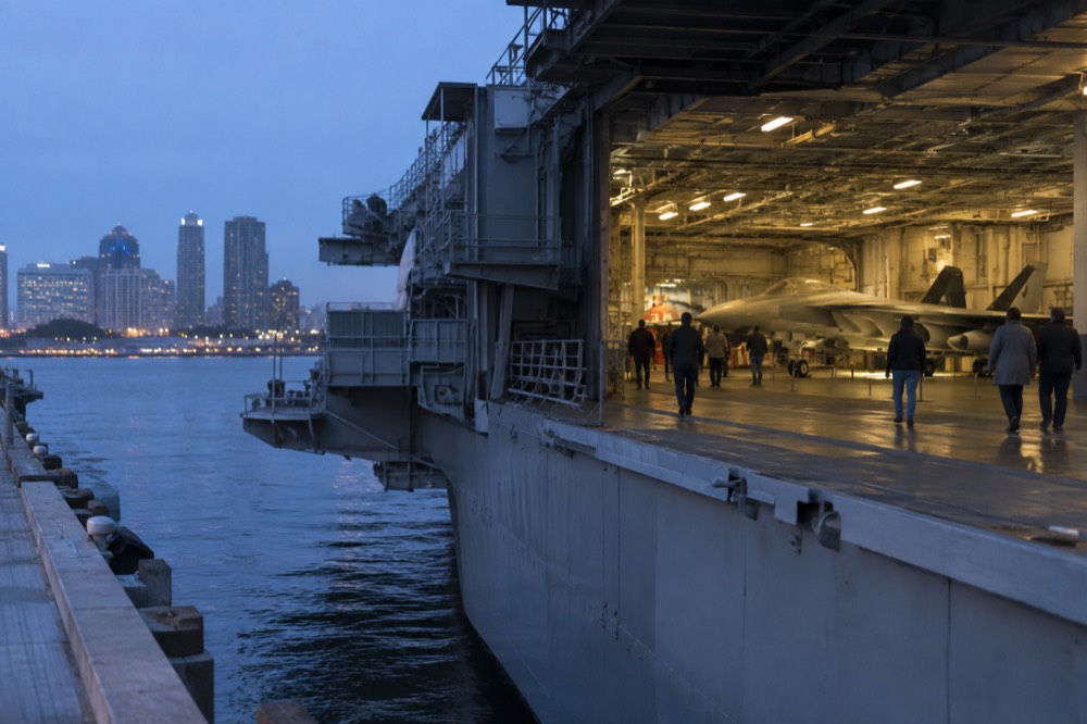 Visitors walking beside a restored fighter jet inside the carrier's wide hangar deck