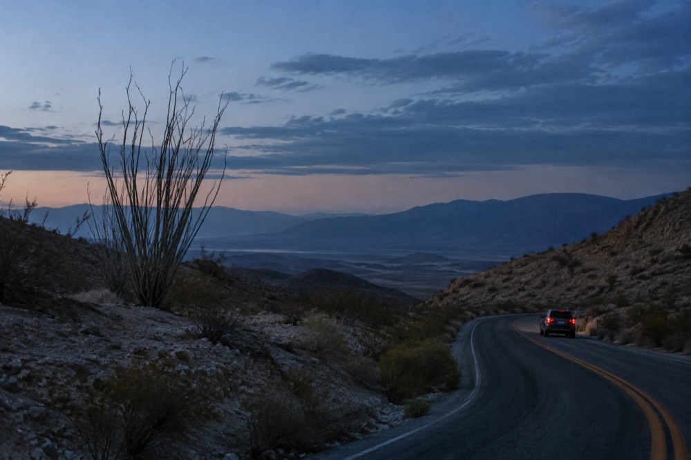 Two-lane highway curving through dry golden hills with a distant desert basin below