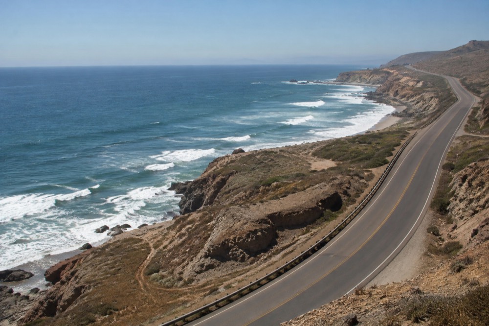 Coastal cliffs and open ocean under a clear sky with a long empty road along the shoreline