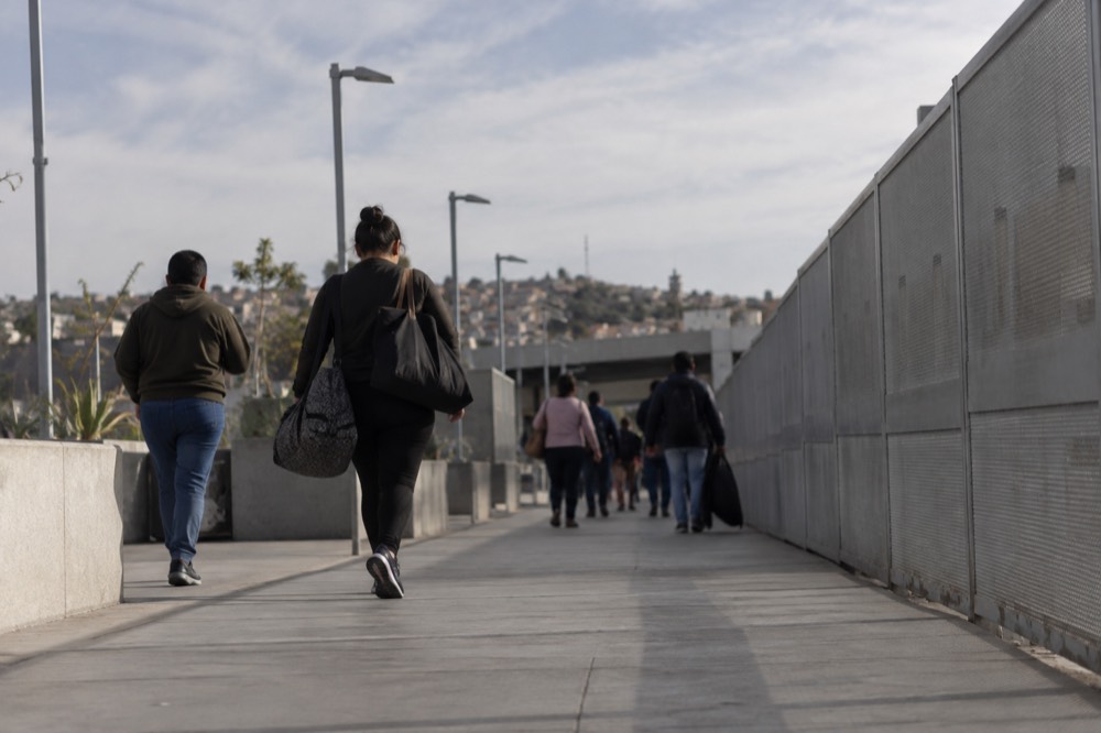 Pedestrian walkway leading toward a border crossing entrance with signage and fencing