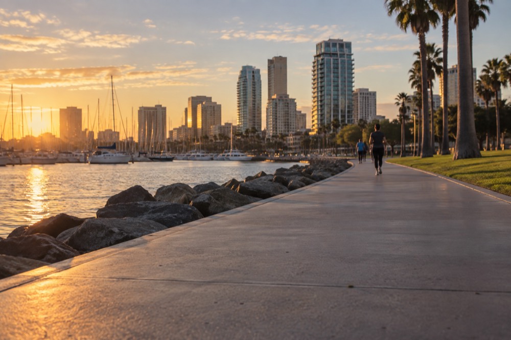 A smooth concrete bayside path curving past sailboats and a park lawn