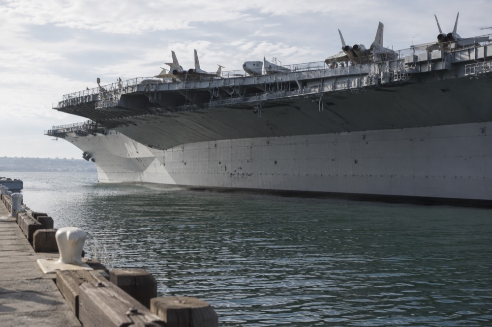 The flight deck of a museum aircraft carrier with jets parked in a row and railings around the deck