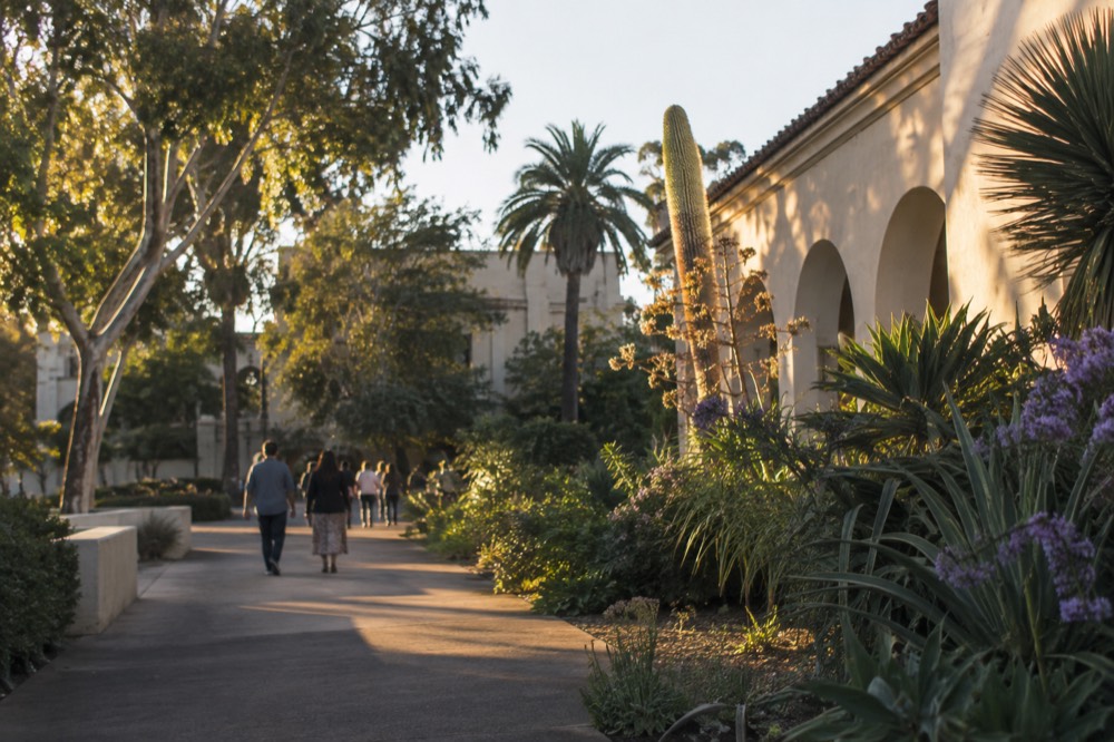 Visitors walking a garden path beside a museum building in Balboa Park