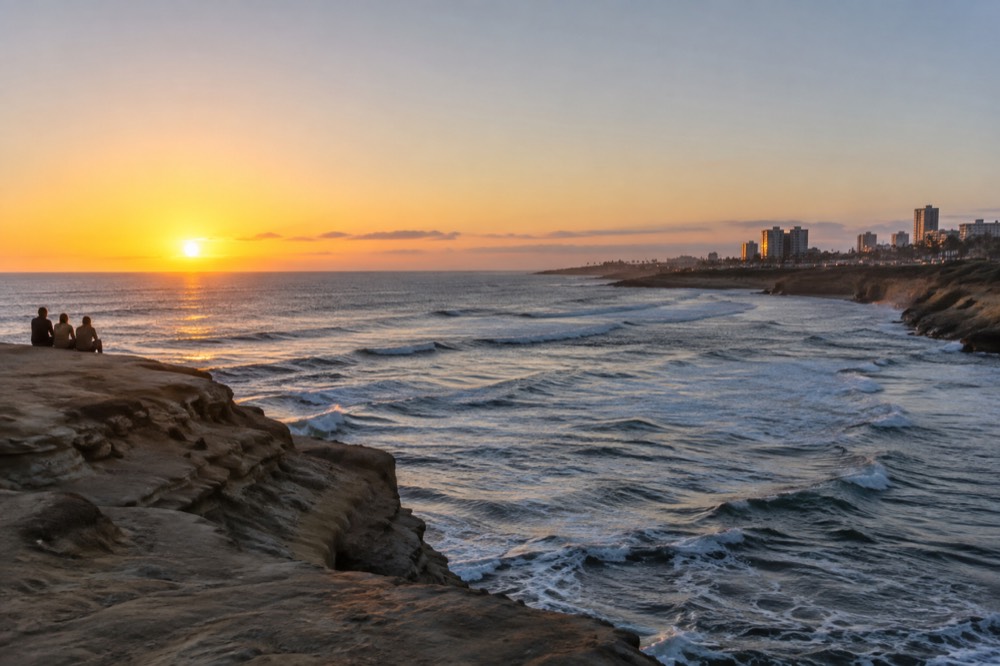 Sun setting over the ocean seen from a sandstone cliff edge with waves below