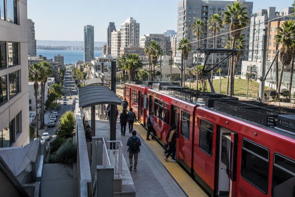 A red San Diego trolley car at a downtown station with passengers boarding