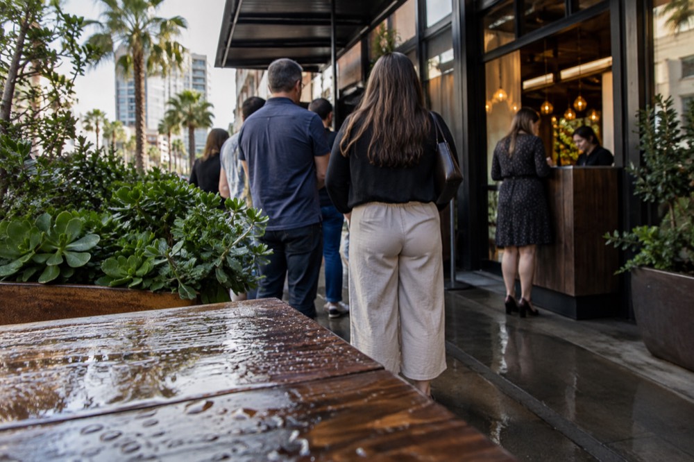 A host stand at a busy restaurant entrance with a small line of waiting diners