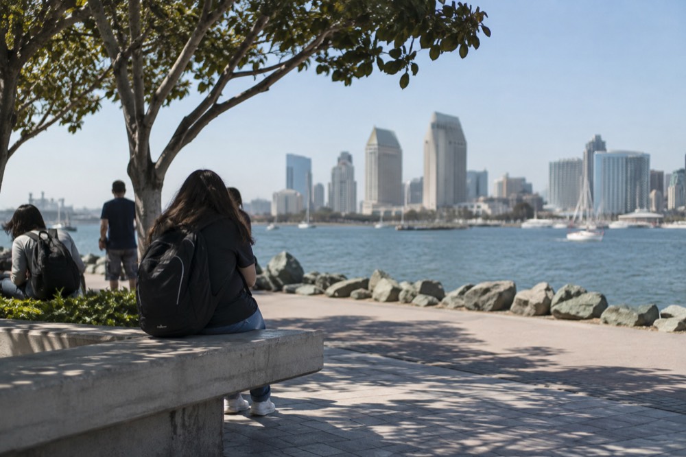 Attendees with backpacks resting on a shaded waterfront promenade near the convention center
