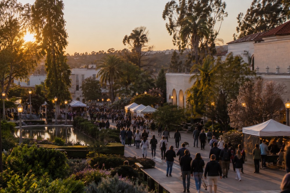 Crowds walking past illuminated museum buildings in Balboa Park during an evening festival