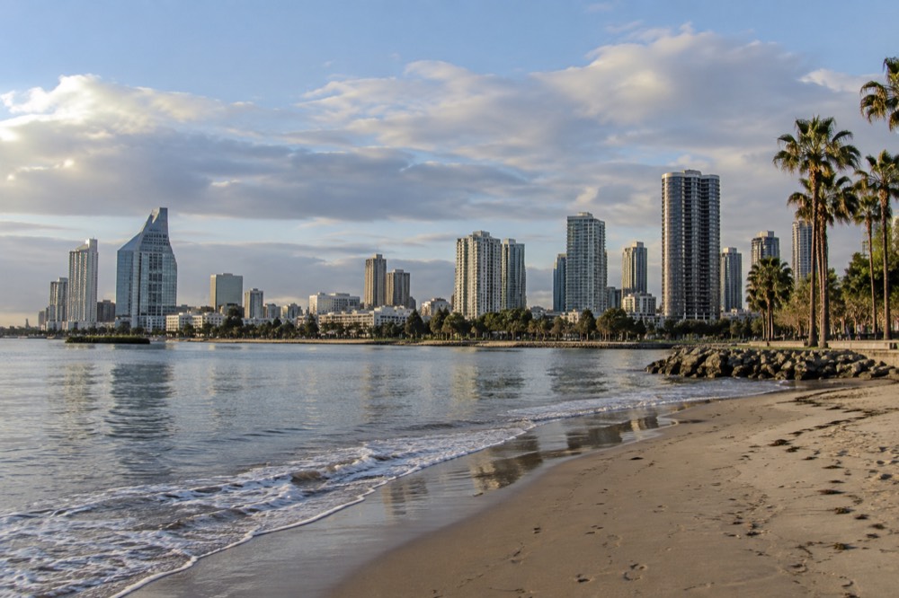 Calm bay water with a sandy beach and palm trees along a walkway