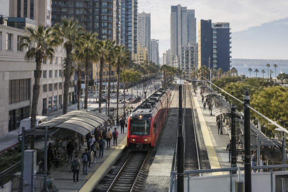 Red trolley arriving at a downtown San Diego station with passengers waiting