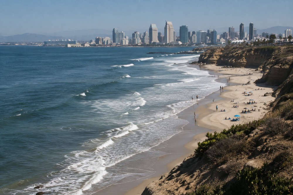 People relaxing on a wide sandy beach with rocky cliffs in the background