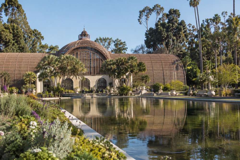 A wooden lath botanical building beside a still reflecting pond surrounded by gardens