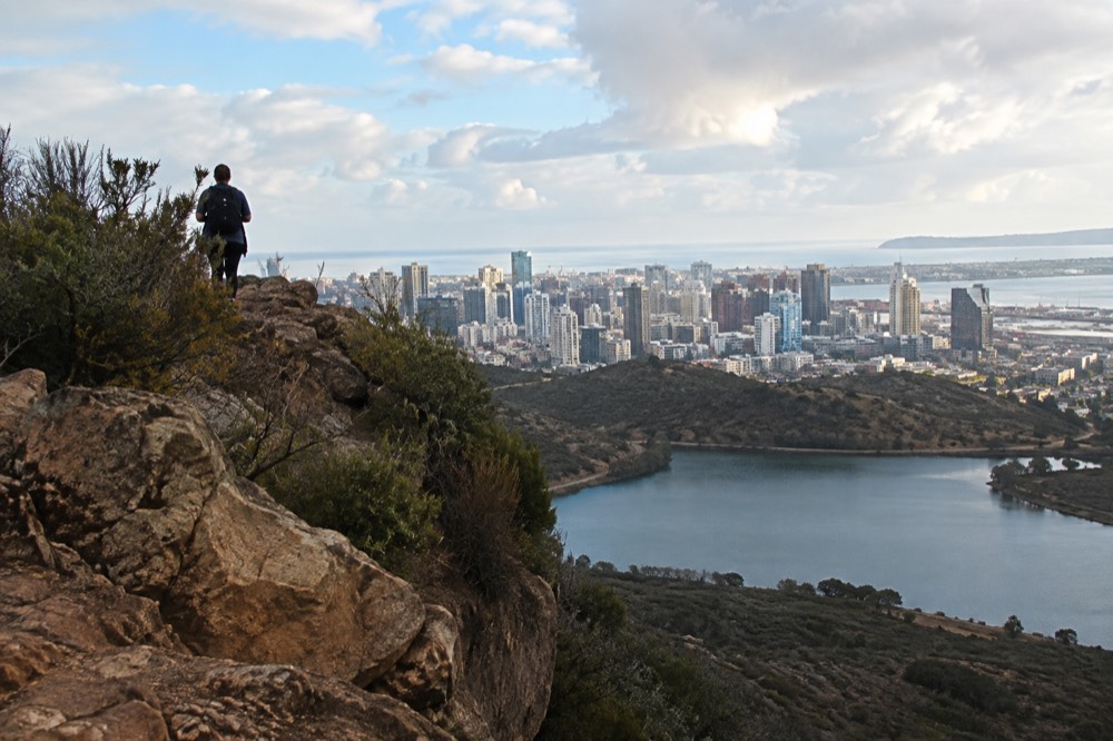 A narrow rock ledge jutting from a chaparral covered mountain above a lake