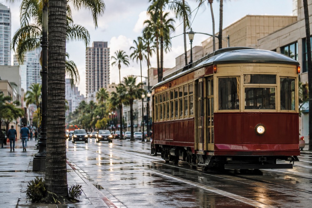 A vintage styled trolley on a downtown street beside palm trees and low buildings