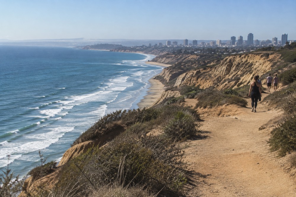 A dirt trail winding along a sandstone cliff above the Pacific Ocean