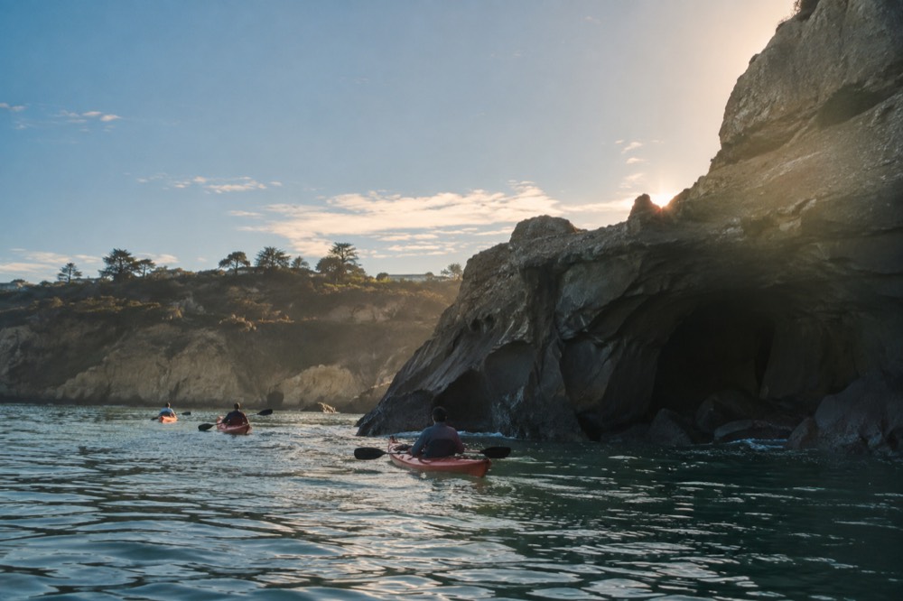 Kayaks floating on calm green water near rocky cliffs along the La Jolla coastline
