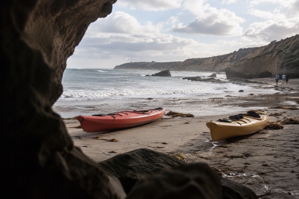Two kayaks resting on wet sand at a wide beach with cliffs in the distance
