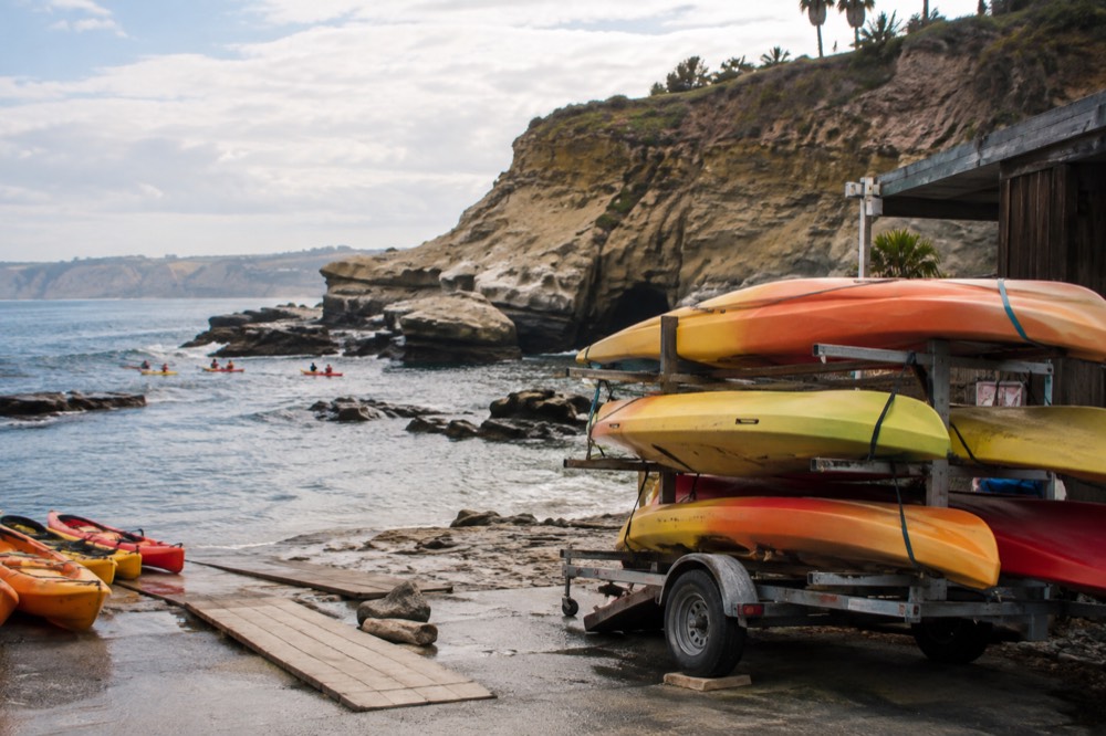 Rented kayaks stacked on a trailer beside a beachside rental shop