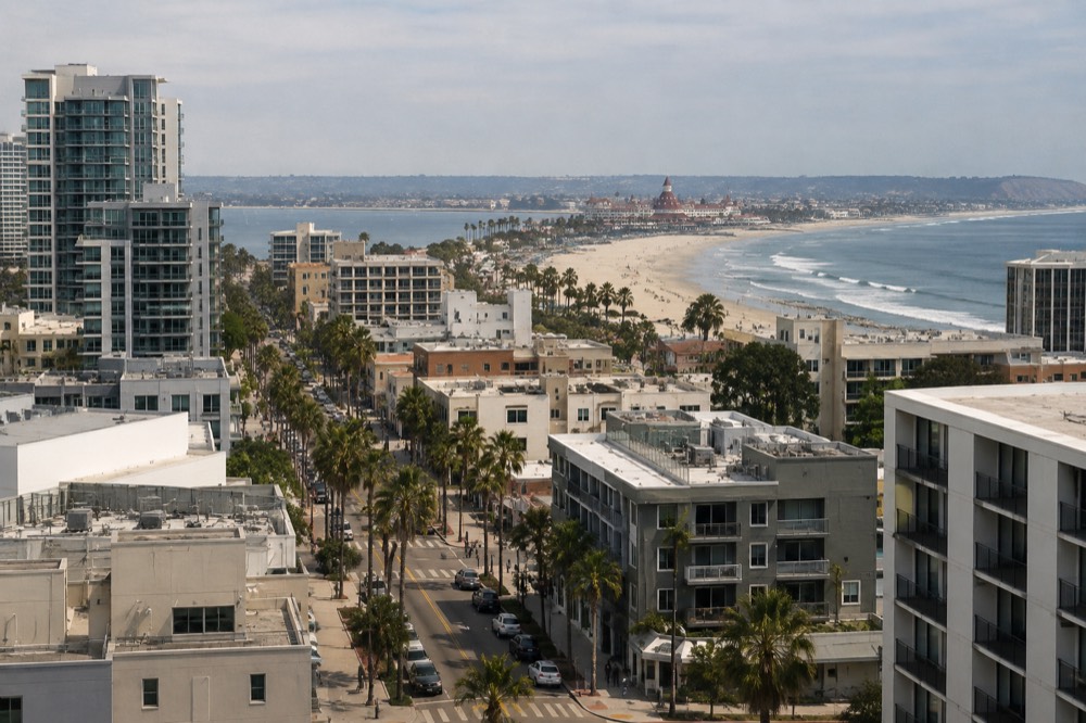 A long sandy beach with gentle waves and a historic red-roofed hotel in the distance