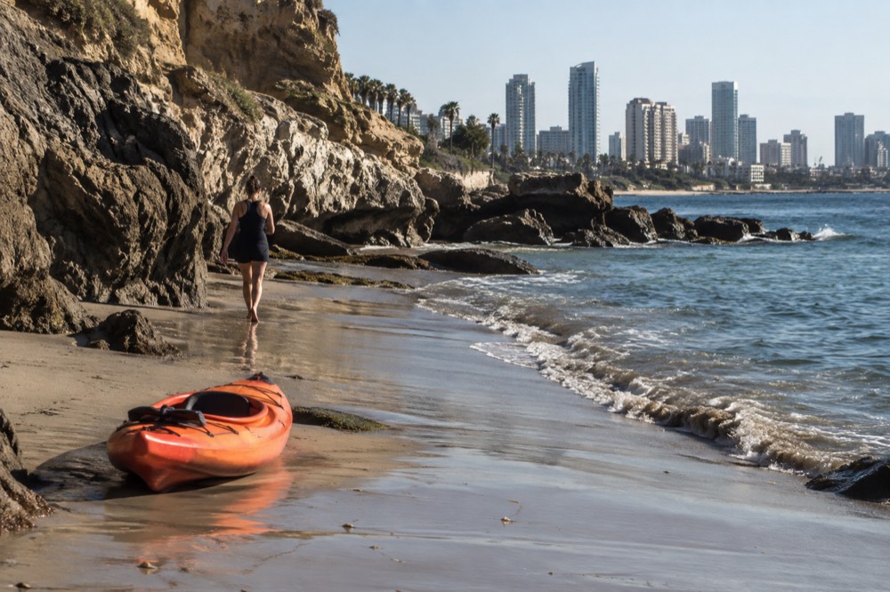 A kayak sitting on wet sand near rocky cliffs above calm green water