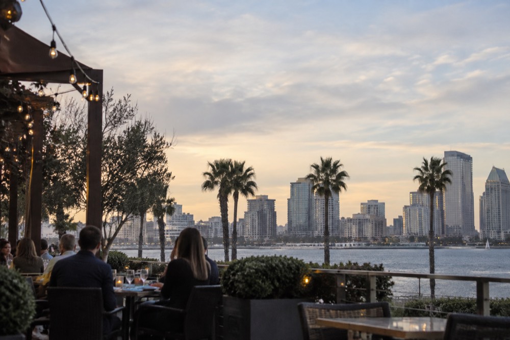 An outdoor patio with string lights and diners at small tables in the early evening