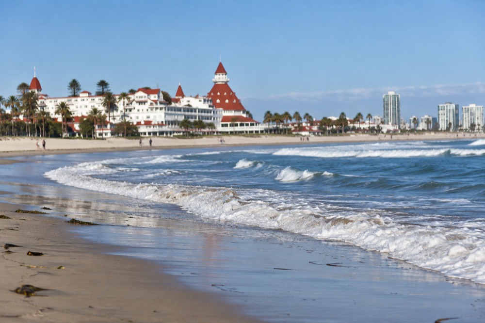 A white historic hotel with red turrets and wide lawns beside the ocean