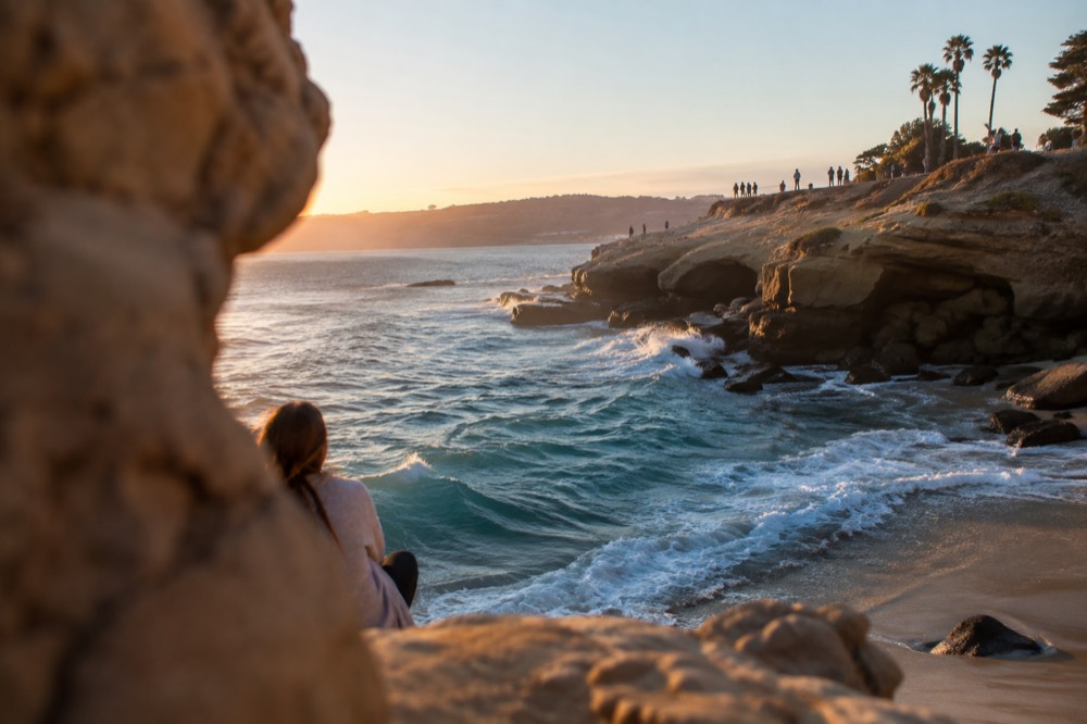Turquoise water breaking against the sandstone cliffs of a La Jolla cove under a clear sky