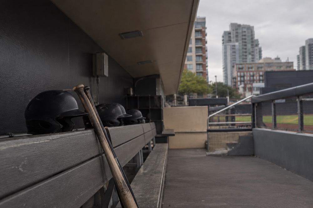 Empty baseball dugout with bats and helmets resting on the bench rail