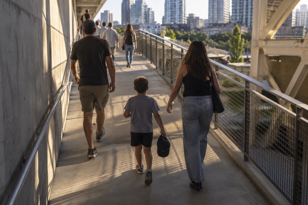 Family walking up a stadium concourse ramp with a child holding a baseball cap