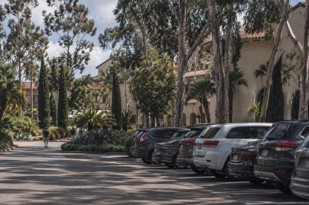 Cars parked in a tree-lined lot beside Spanish-style museum buildings in Balboa Park