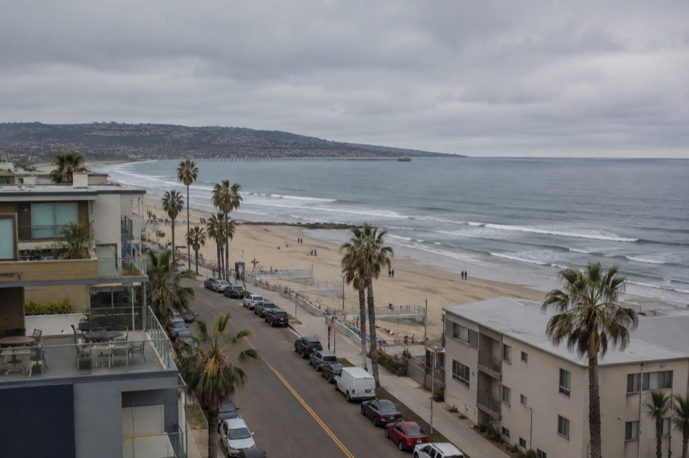 Cars parked along a beachfront street with sand and ocean beyond