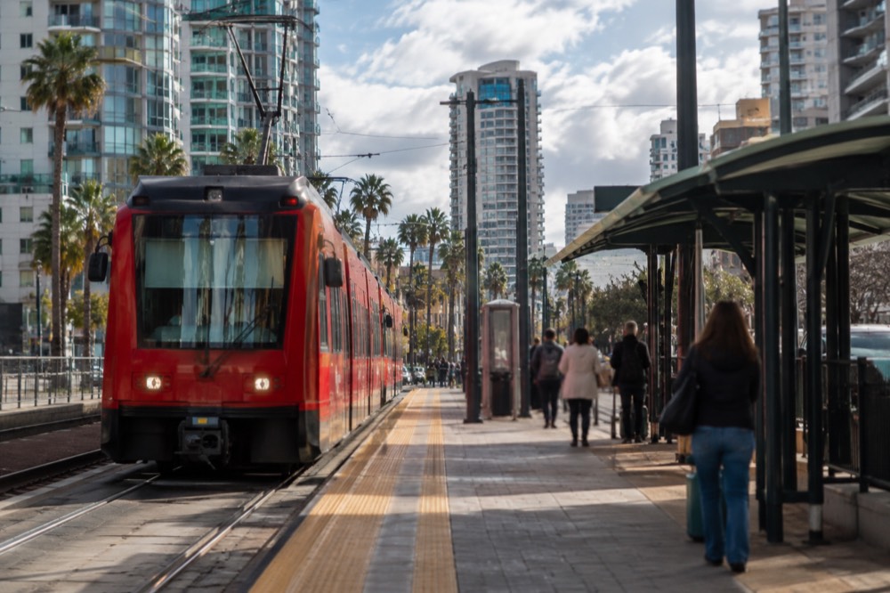 A red trolley car at a downtown station with passengers waiting on the platform