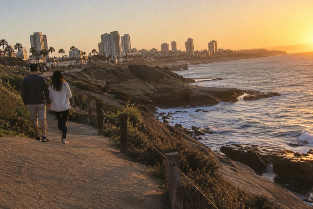 A couple walking along a oceanfront cliff path at golden hour with waves below