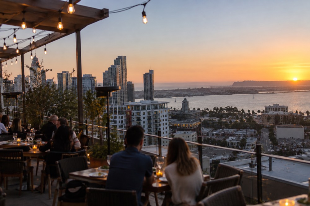 An outdoor restaurant terrace with string lights above tables at dusk