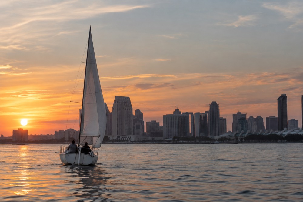 A small sailboat with two people aboard on calm bay water at sunset